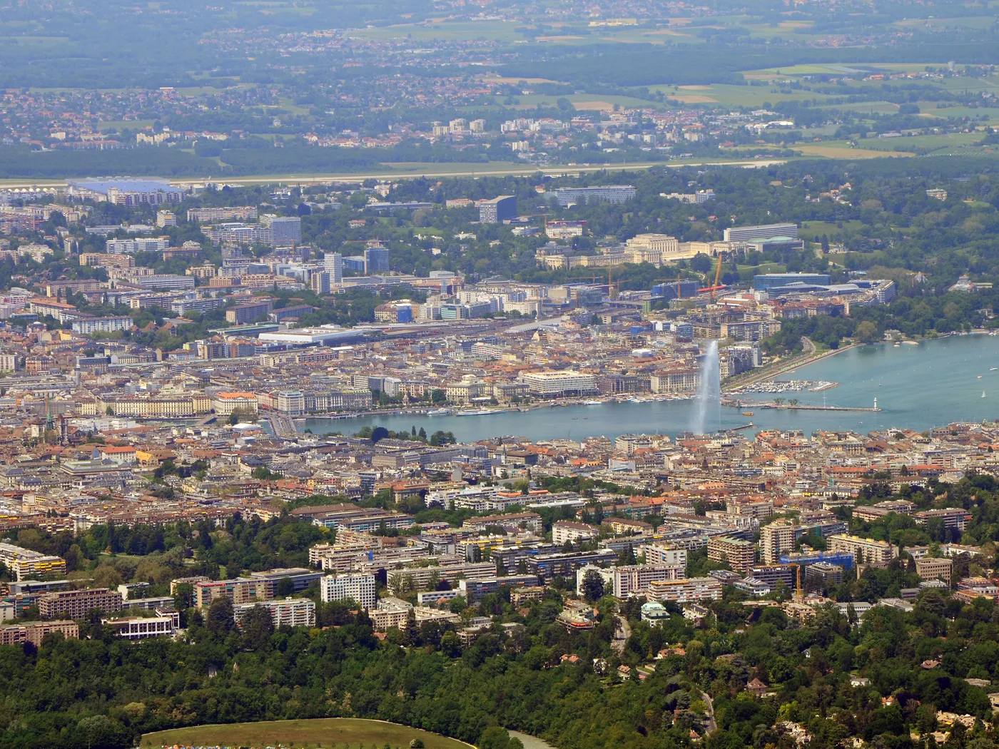 Genève vue depuis le Salève : la rade et le jet d'eau au centre, les quartiers denses de part et d'autre du lac, et la plaine jusqu'à l'aéroport