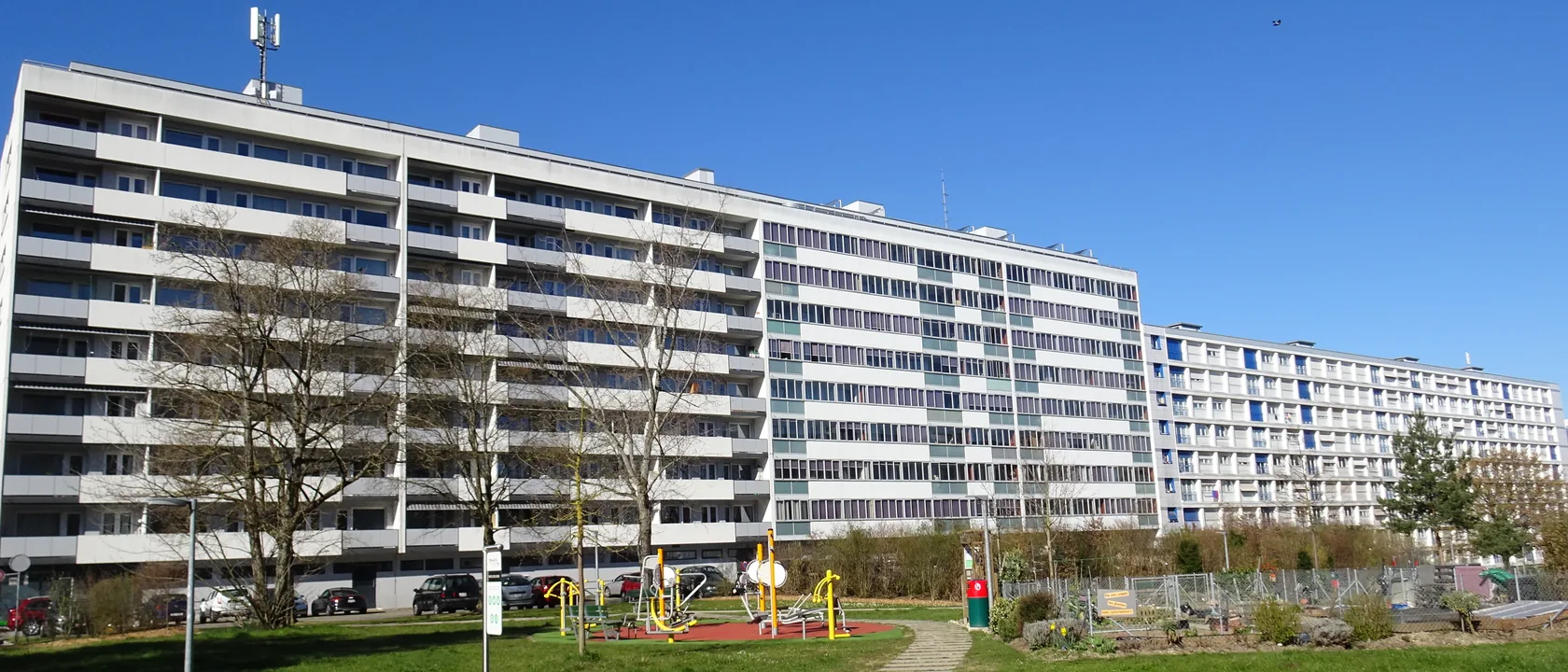 Barres d'immeubles de l'avenue du Gros-Chêne à Onex vues depuis le parc : copropriétés des années 1960 à longs balcons filants, dont les sous-sols sont équipés de pompes de relevage