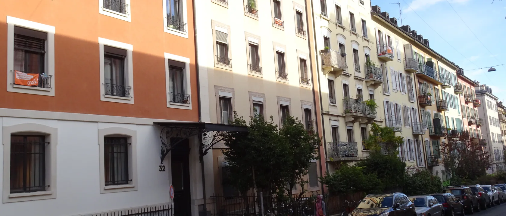 Rue du Jura à La Servette, Genève : alignement d'immeubles locatifs anciens aux façades ocre et crème, balcons en fer forgé et volets, typologie desservie par SOS Relevage pour les régies